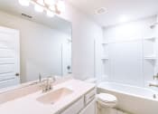 Thumbnail 14 of 16 - Apartments in Gallatin, TN, for Rent - The Gardens at Preston Park - White Bathroom with Full Tub and Shower, Built-In Shelves, White Cabinetry, Vanity with Quartz Countertop and Sink, Mounted Mirror, and Bright Lighting.