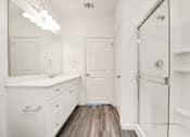 Thumbnail 34 of 41 - 3 Bedroom Homes for Rent in Houston TX - Imperial Forest - Bright, White-Walled Bathroom with a Glass Shower, White Cabinetry, Mirror, and Wood-Style Flooring