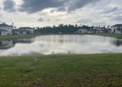 Thumbnail 30 of 56 - A serene landscape with a lake, houses, and trees under a cloudy sky.
