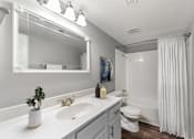Thumbnail 9 of 12 - A white bathroom with a sink, mirror, toilet, and shower.