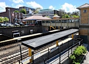 Thumbnail 20 of 25 - A train station with a black roof and a yellow fence.