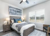 Thumbnail 12 of 39 - Four-BR Homes for Rent in Katy, TX - Villas at Sunterra - Bedroom with a Large Window, a Ceiling Fan, a Large Bed, Two Nightstands with Lamps, Wood-Style Flooring, and Stylish Decor