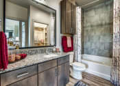 Thumbnail 3 of 18 - 	Grand Prairie, TX Apartments - Waters Edge at Mansfield - Bathroom With Wood-Style Flooring, Ceramic Tub, Framed Vanity Mirrors With Decorative Lighting, and Granite Countertop.
