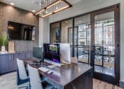 Thumbnail 8 of 18 - 	Pet Friendly Apartments in Grand Prairie, TX - Waters Edge at Mansfield - Private Business Center With Table, Chairs, Computers, Mounted TV, Pendant Light Fixture, and Puck Lighting.