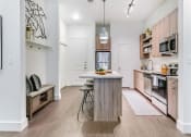 Thumbnail 14 of 40 - Apartments for Rent in Rowlett, TX - Village of Rowlett - Kitchen with Wood-Style Flooring, Granite Countertops, Wood-Tone Cabinetry, Stainless Steel Appliances, Kitchen Island/Breakfast Bar, Bar-Style Stools, Pendant Lights, Pantry, Storage Shelves, and Bench Seat.