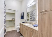 Thumbnail 15 of 40 - One-Bedroom Apartments in Rowlett, TX - Village of Rowlett - Bathroom with Wood-Style Flooring, Granite Vanity Countertop, Large Mirror, Wood-Tone Cabinetry, and Large Closet with Shelves and Hanger Bars.