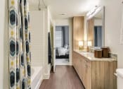 Thumbnail 17 of 40 - Rowlett, TX Apartments for Rent - Village of Rowlett - Bathroom With Wood-Style Flooring, Shower and Tub Combo, Large Vanity Mirror, Wide Granite Countertop with Sink and Wood-Style Cabinets