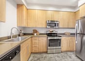 Thumbnail 1 of 18 - 2 Bedroom Modern Apartments in Long Beach, CA - Urban Village - Kitchen with Stained Concrete Flooring, Light Wood Cabinetry, Stainless Steel Appliances, and Quartz Countertops.
