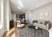 Thumbnail 8 of 18 - 1 Bedroom Modern Apartments in Long Beach, CA - Urban Village - Living Room with Vinyl Plank Flooring, Area Rug, Sofa, Armchair, Coffee Table, and Large Windows.