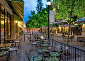 Thumbnail 16 of 24 - A city street with tables and chairs is lit up at night.