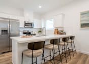 Thumbnail 2 of 20 - Dog-Friendly Townhomes in Tolleson, AZ - Villas at 91st - Bright White Kitchen With Quartz Island Seating, Shaker Cabinets, and Stainless Steel Refrigerator Appliances.