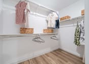 Thumbnail 16 of 45 - A white closet with clothes hanging and baskets on the shelf.