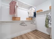 Thumbnail 9 of 20 - A white closet with clothes hanging and baskets on the shelf.