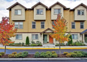 Thumbnail 8 of 14 - Apartments for Rent in Kenmore WA - Northshore Townhomes - Property Exterior Surrounded by Trees, with Street View, Featuring Brightly-Colored Doors, Tan and Yellow Walls, Brown Trim, and Multiple Sto