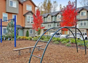 Thumbnail 11 of 14 - Kenmore WA Apartments - Northshore Townhomes - Outdoor Playground with Metal Bars, Swings, and Surrounding Trees