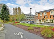 Thumbnail 12 of 14 - Kenmore, WA, Apartments for Rent - Northshore Townhomes - Bike Path and Building Exterior with View of Parking Lot and Surrounded by Beautiful Landscaping and Trees.