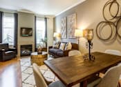 Thumbnail 3 of 16 - Apartments for Rent in Kenmore, WA - Northshore Townhomes - Furnished Living And Dining Area With Fireplace, Large Windows, Wood Flooring, Sofa Seating, And Decorative Wall Art.