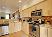 Thumbnail 1 of 14 - Kenmore WA Apartments for Rent - Northshore Townhomes - Modern Kitchen with Stainless Steel Appliances, Granite Countertops, Tan Tile Backsplash, Wood-Style Cabinetry, and L-Shape