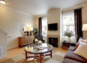 Thumbnail 2 of 14 - 2 Bedroom Apartments in Kenmore WA - Northshore Townhomes - Living Room with a Fireplace, a Couch, a Glass Circular Coffee Table, Wooden Cabinets, Plants, Windows, and Wood-Style Flooring, and View of