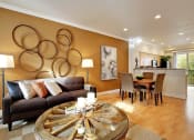 Thumbnail 3 of 14 - Kenmore, WA, Apartments - Northshore Townhomes - Living Room with Hardwood Flooring, Couch, Round Coffee Table, Standing Lamps, Mustard Yellow Accent Wall, Wall Art, and View of Dining Area and Kitchen.