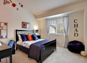 Thumbnail 4 of 14 - Three-Bedroom Apartments in Kenmore, WA - Northshore Townhomes - Bedroom with Carpeted Flooring, Bed, Nightstand with Lamp, Desk Chair, Bean Bag, Vaulted Ceiling, and Large Window.