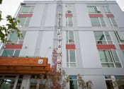 Thumbnail 13 of 20 - South Seattle, WA, Apartments - Greenhouse - Property Exterior with Grey Walls, Red and Wooden Details, and Trees.