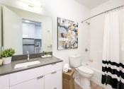 Thumbnail 9 of 54 - Fremont, WA Apartments - Inspire Fremont - Bathroom with a Bathtub, Granite-Style Sink, and a Large Mirror