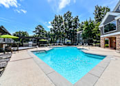 Thumbnail 1 of 17 - A large swimming pool surrounded by a concrete patio and lounge chairs.
