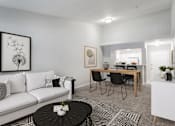 Thumbnail 10 of 39 - A living room with a white couch, a coffee table, and a dining table with chairs.