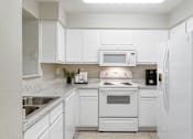 Thumbnail 6 of 39 - A white kitchen with a sink, stove, and refrigerator.