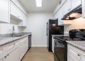 Thumbnail 25 of 33 - Whitney Manor Apartments in Gretna, LA photo of a kitchen with white cabinets and black appliances