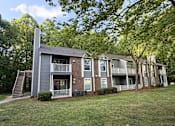 Thumbnail 13 of 25 - Apartment building with a grey and brown exterior and a tree in front.