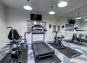 Thumbnail 19 of 35 - Two-Bedroom Apartments in Everett, Washington - Woodbrook - Fitness Center with Elliptical Machine, Treadmill, Stationary Bike, Mirror Wall, TV, and Window.
