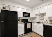 Thumbnail 1 of 23 - A black refrigerator sits next to a black stove in a kitchen with white cabinets.