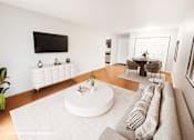 Thumbnail 3 of 20 - A living room with a white couch and a television on the wall.