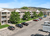 Thumbnail 8 of 9 - A parking lot with cars and a trailer in front of apartment buildings.