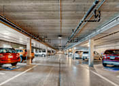 Thumbnail 6 of 9 - A parking garage with cars parked on both sides of the aisle.