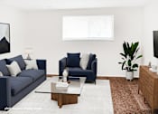Thumbnail 16 of 32 - A living room with a blue couch, a blue chair, a glass coffee table, a rug, a plant, and a TV.