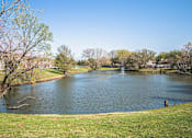 Thumbnail 18 of 23 - A lake in a park with a fountain in the middle.