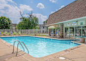 Thumbnail 16 of 22 - A swimming pool with a diving board and a building in the background.