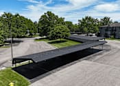 Thumbnail 34 of 41 - A black covered walkway leads from a parking lot to a building.