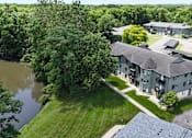 Thumbnail 38 of 41 - A large building with a grey roof is surrounded by trees and a body of water.