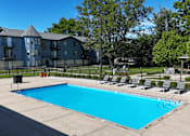 Thumbnail 27 of 41 - A large swimming pool surrounded by chairs and a building in the background.