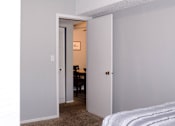 Thumbnail 16 of 17 - A white door opens to a room with a desk and a bed.