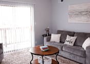 Thumbnail 6 of 17 - A living room with a grey couch and a round table with a book on it.
