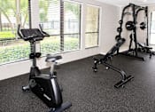 Thumbnail 10 of 18 - A black exercise bike is in a room with a weight rack.
