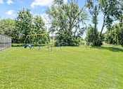 Thumbnail 26 of 32 - A playground with a yellow swing set in a grassy area.