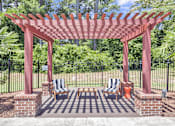 Thumbnail 24 of 33 - A red pergola with two chairs and a table is in the foreground of a garden.