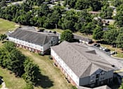 Thumbnail 33 of 33 - A large white building with a black roof is surrounded by trees and smaller buildings.