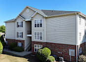 Thumbnail 28 of 33 - A two-story apartment building with a red brick base and beige siding.